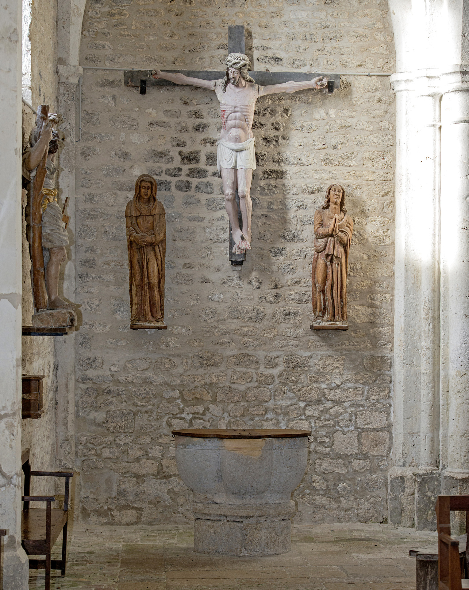 Travée 15 de L'église avec le Christ entouré de Marie et Jean. En dessous les fonts baptismaux. Tout à gauche une statue de St Christophe.